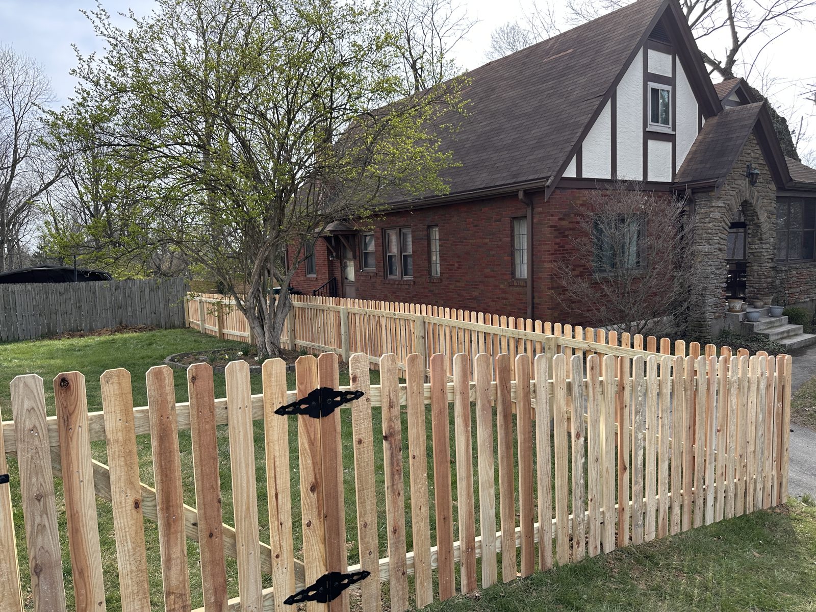 Wood picket fence in front of a brick Tudor home