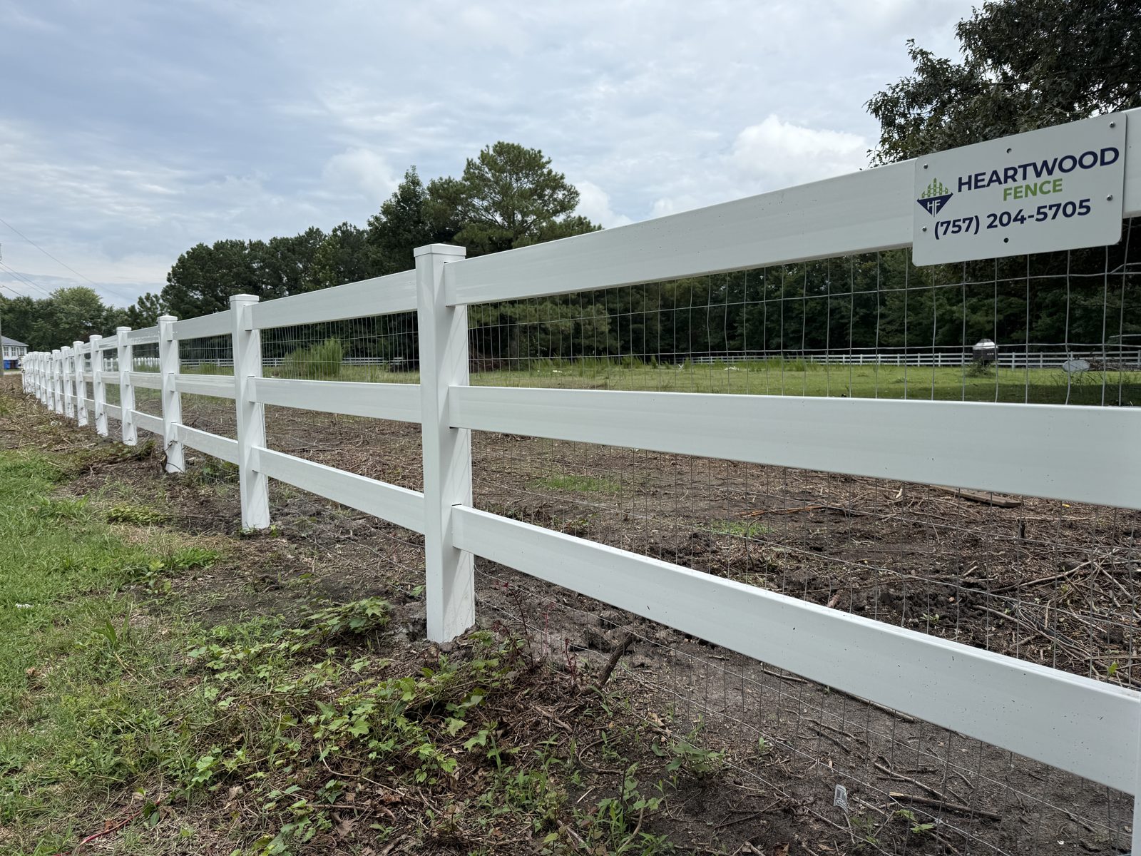 White vinyl ranch rail fence with a Heartwood Fence sign
