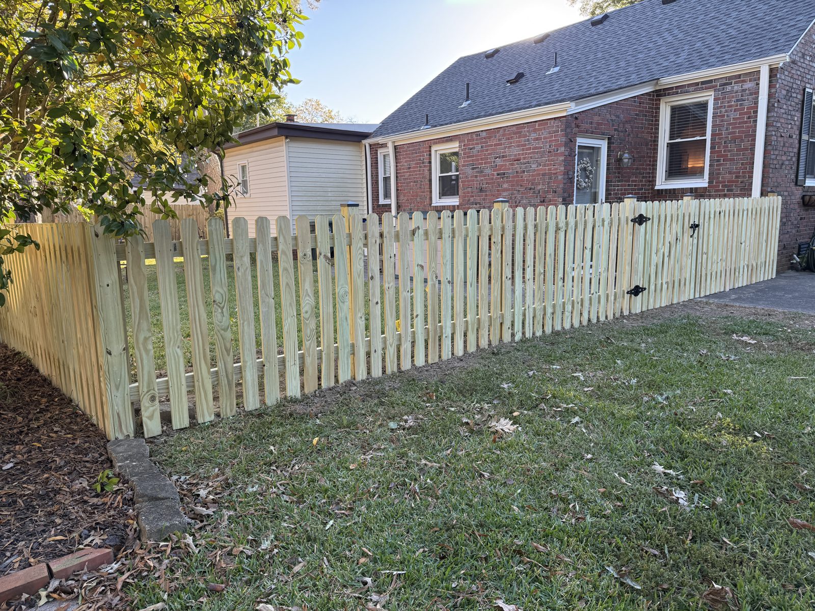 Spaced wood picket fence in front of a brick home